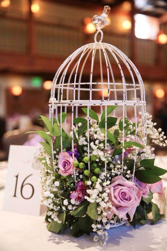 a white shabby chic cage with pink and purple roses, baby's breath, greenery is a cool wedding centerpiece