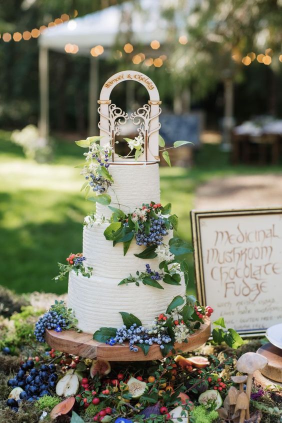 a white wedding cake with greenery and berries and a creative wedding cake topper for a LOTR wedding