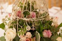 an opened birdcage stuffed with pink and white roses and greenery is a lovely wedding centerpiece