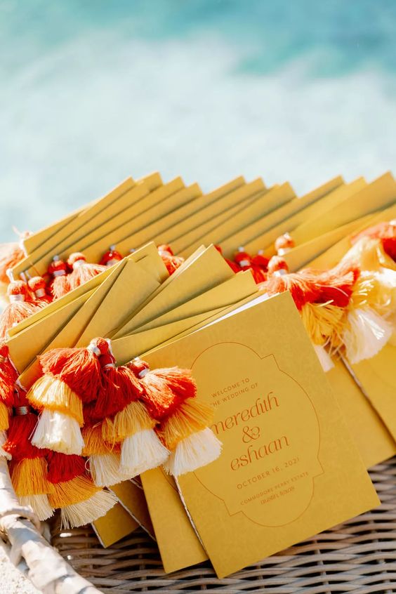mustard-colored wedding programs with colorful tassels are lovely for a modern playful or boho wedding, they will add color and interest