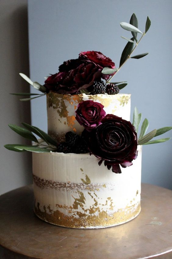 a gorgeous semi naked wedding cake with gold leaf, dark burgundy blooms, greenery and blackberries