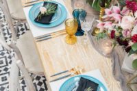 08 The tablescape features blue plates, blue and gold glasses, black candles in gold candle holders and various lush florals