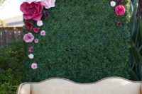 08 a chic photo booth with a green wall topped with paper flowers in pink and fuchsia colors, and a refined sofa
