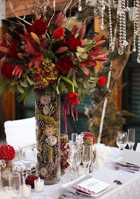 a tall vase filled with moss and pinecones and with red blooms brings a winter feel
