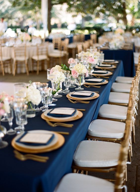 a chic table setting with navy napkins and a tablecloth, gold cutlery and chargers for a chic look