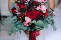 19 a bold wedding bouquet with dark leaves, red and pink blooms, eucalyptus and other greenery and red ribbons
