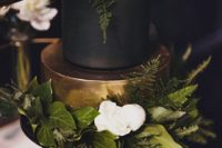 19 a gold and black wedding cakewith lush greenery and a couple of white flowers