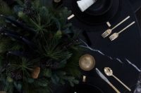 20 a moody winter setting with black plates, gold goblets, evergreens and black candles
