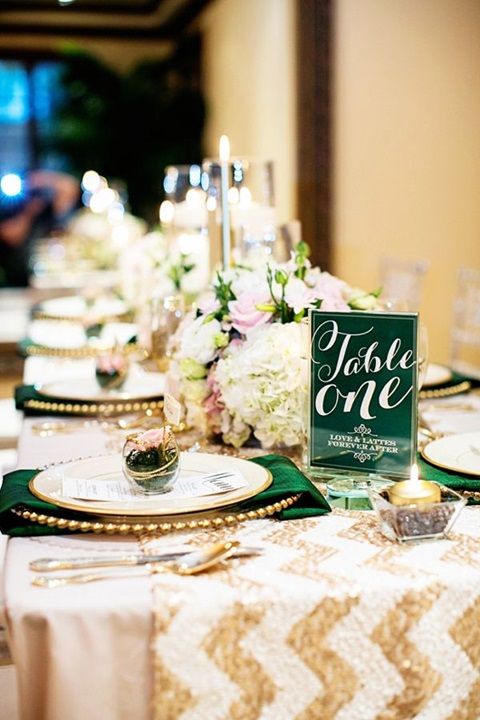 a chic table setting with a chevron gold table runner, emerald napkins and table numbes, gold cutlery and succulents