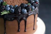 23 a naked chocolate cake with chocolate drip, blackberries and blueberries and touches of evergreens