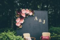 23 a wedding photo booth with a black wall topped with pink and burgundy flowers and refined chairs