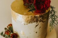 26 a chic winter wedding cake decorated with gold leaf, evergreens and red roses
