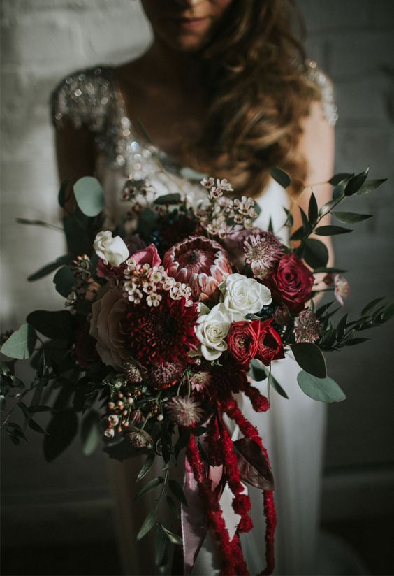 a textural winter wedding bouquet with foliage, red blooms, cascading amaranthus and dahlias