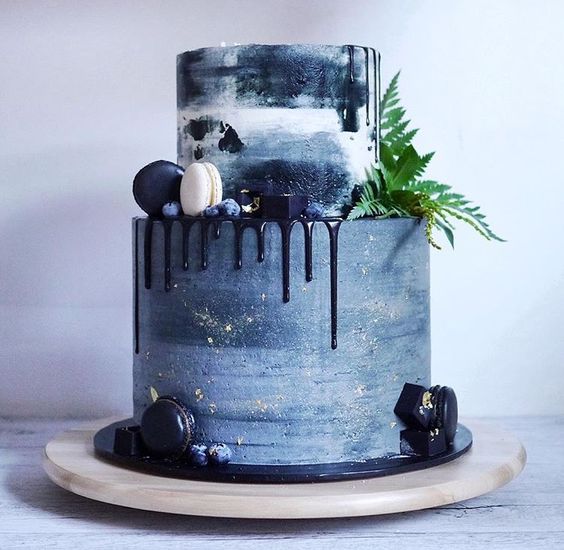 a watercolor blue wedding cake looks dramatic and moody with navy drip, fern and macarons in navy and white