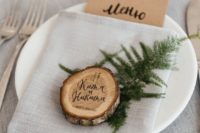 02 a cozy rustic place setting with a grey tablecloth and napkin, a wood slice, evergreens and a kraft paper menu
