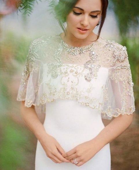 a heavily beaded and embroidered capelet over an off the shoulder white wedding dress