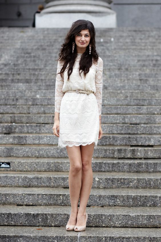 an ivory lace wedding dress with long sleeves and a leather belt on the waist, statement earrings and nude shoes