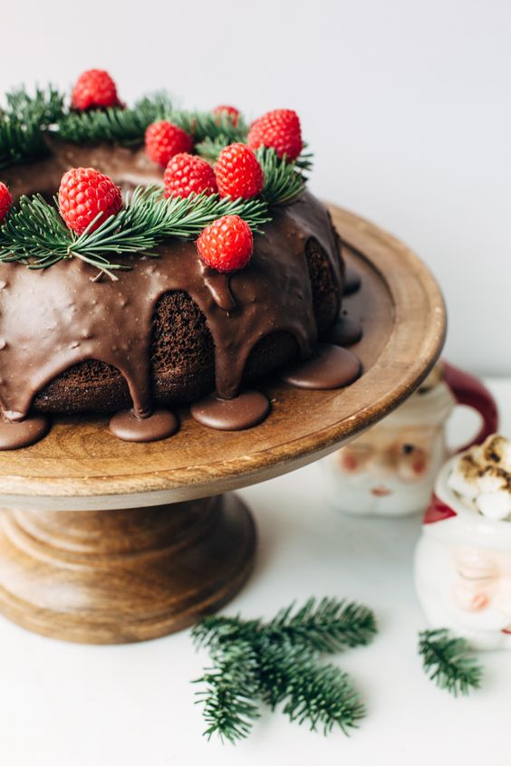 a chocolate wreath wedding cake with chocolate drip, evergreens and raspberries