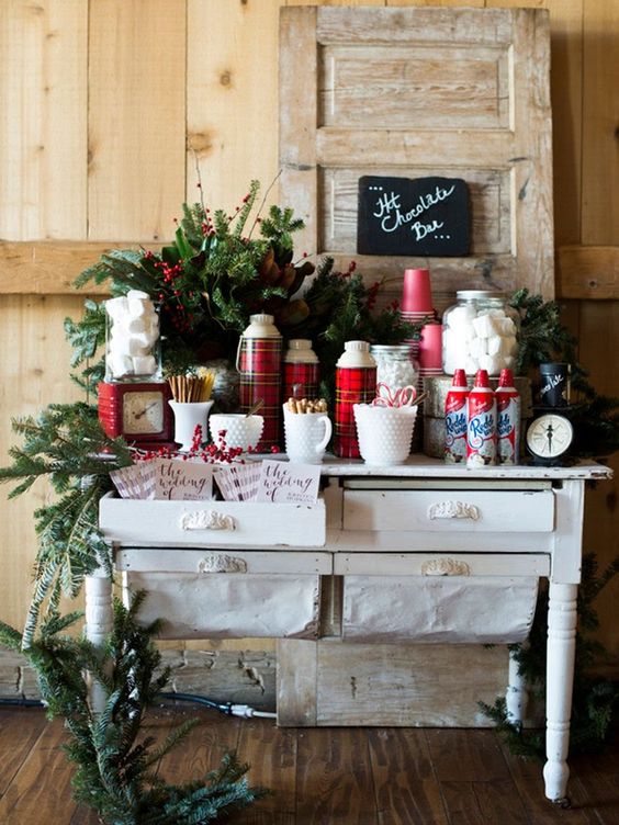 a gorgeous hot chocolate bar with an evergreen garland, plaid thermoses, lots of sweets for eating them