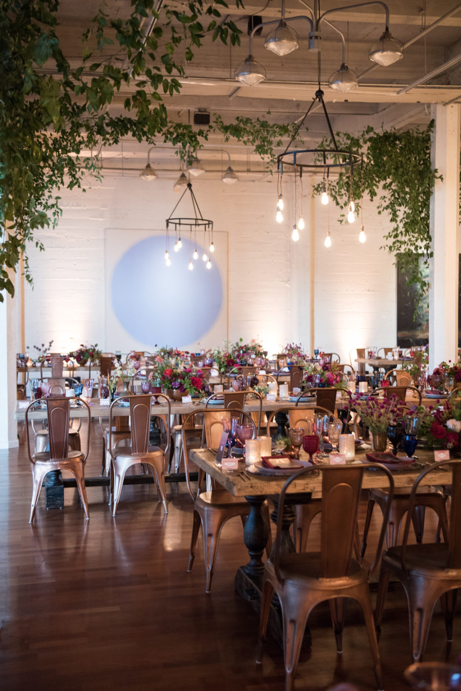 The wedding reception was done with vintage wooden tables, metal chairs, industrial chandeliers and greenery