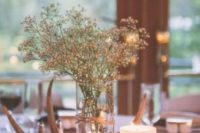 12 a cozy rustic wedding centerpiece with a wood slice, a candle, antlers and some baby’s breath in a vase