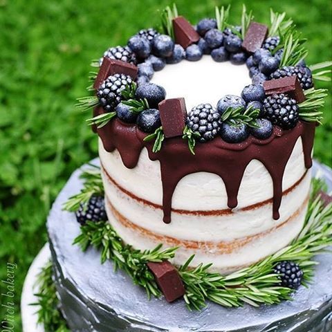 a semi-naked wedding cake with chocolate dripping, topped with evergreens, chocolate, blueberries and blackberries