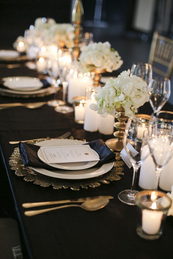 a stunning black and gold wedding tablescape with gold sunburst chargers, gold candle holders and vases