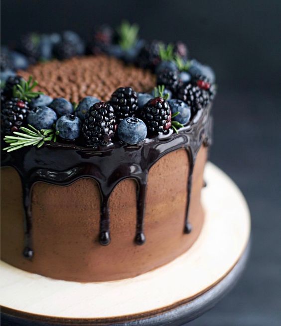 a naked chocolate wedding cake with dark chocolate dripping, topped with rosemary, blueberries and blackberries