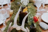 17 a moss table runner with candles, wildflowers in bottles and antlers for a woodland-inspired wedding