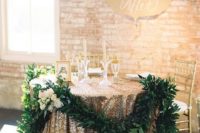 19 a gold glitter tablecloth and a greenery garland with blooms for highlighting a sweetheart table