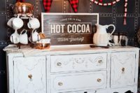19 a gorgeous hot cocoa bar of a vintage sideboard, a plaid banner and mugs with knit cozies