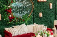 21 a wedding lounge with a greenery wall, lush greenery and red roses and a red velvet sofa