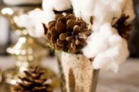 23 a wedding centerpiece with a metallic vase with cotton and pinecones for a winter wedding