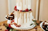 a Christmas wedding cake wityh gold drip, sugared berries, a white bloom and greenery is a very refined dessert