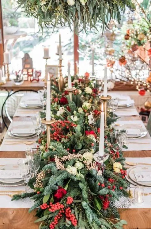 a Christmas wedding tablescape with a greenery and fir runner, with berries and red roses, candles and gold cutlery