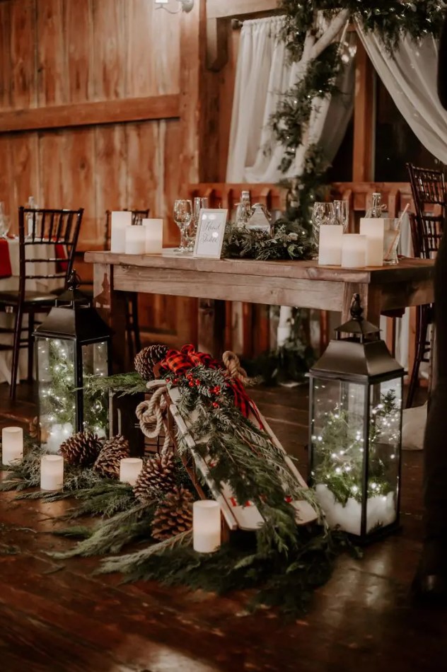 a beautiful and cozy Christmas wedding sweetheart table with evergreen decor, pinecones, candles, candle lanterns and plaid fabric
