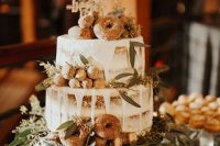 a boho naked wedding cake with creamy drip, greenery, donuts and candies plus a calligraphy topper
