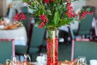 a bold Christmas centerpiece of a tall vase filled with red ornaments, greenery, berries, red roses, twigs is very elegant and chic