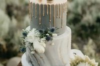 a bold wedding cake with a grey and grey marble tier, gold drip, white blooms, thistles and fun bunny cake toppers