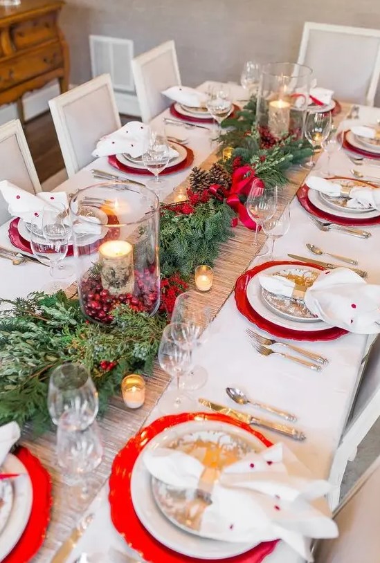 a bright Christmas wedding table with red chargers, an vergreen and pinecone runner, cranberries and birch bark candles, printed plates and polka dot napkins