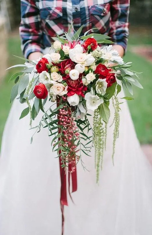 a cascading Christmas wedding bouquet of red and white blooms, foliage and berries and bright ribbons