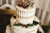 a classic Christmas wedding cake with creamy drip, evergreens, pinecones, berries and a gold calligraphy topper
