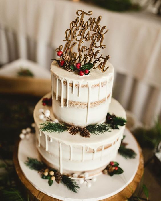 a classic Christmas wedding cake with creamy drip, evergreens, pinecones, berries and a gold calligraphy topper