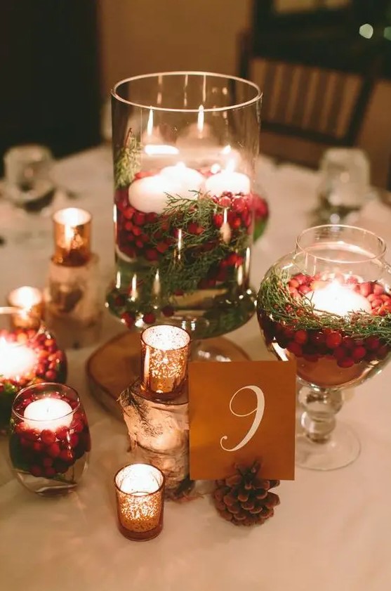a cozy traditional Christmas wedding centerpiece of pinecones, mercury glass candle holders and jars with evergreens, cranberries and candles