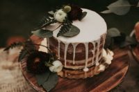 a delicate naked wedding cake with creamy drip, greenery, white blooms is a cool and catchy idea