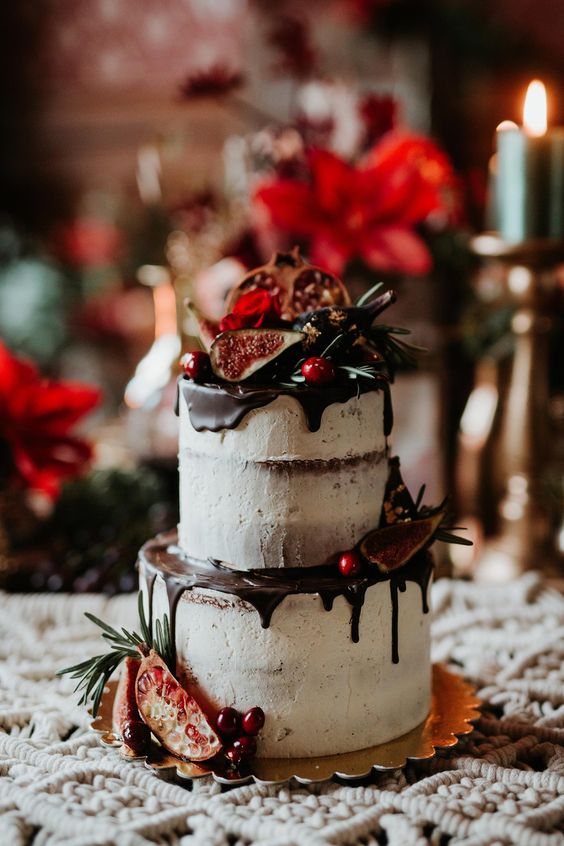 a delicious Christmas wedding cake with chocolate drip, pomegranates on top and some berries and greenery