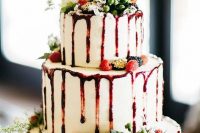a fantastic Christmas drip wedding cake with berry sauce, fresh berries, greenery and a white bloom on top is wow