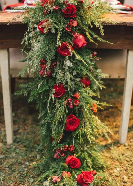 a lush evergreen table runner with red roses for a rustic winter wedding