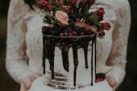 a mini wedding cake with chocolate drip, blackberries, pomegranate seeds, greenery, blush and red blooms
