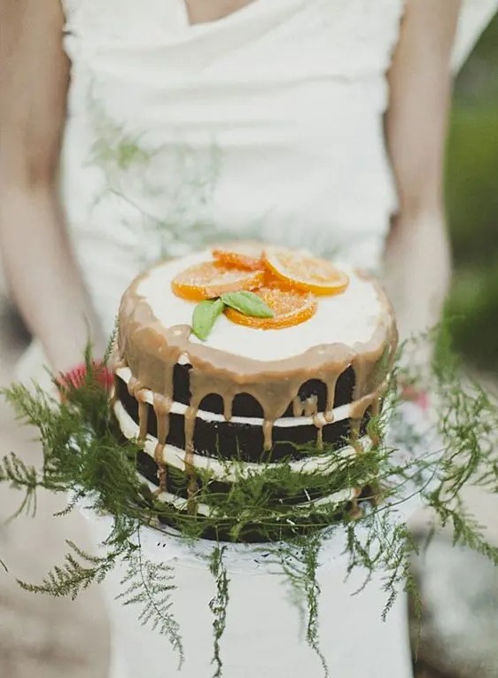 a naked wedding cake with caramel dripping, ferns and citrus slices